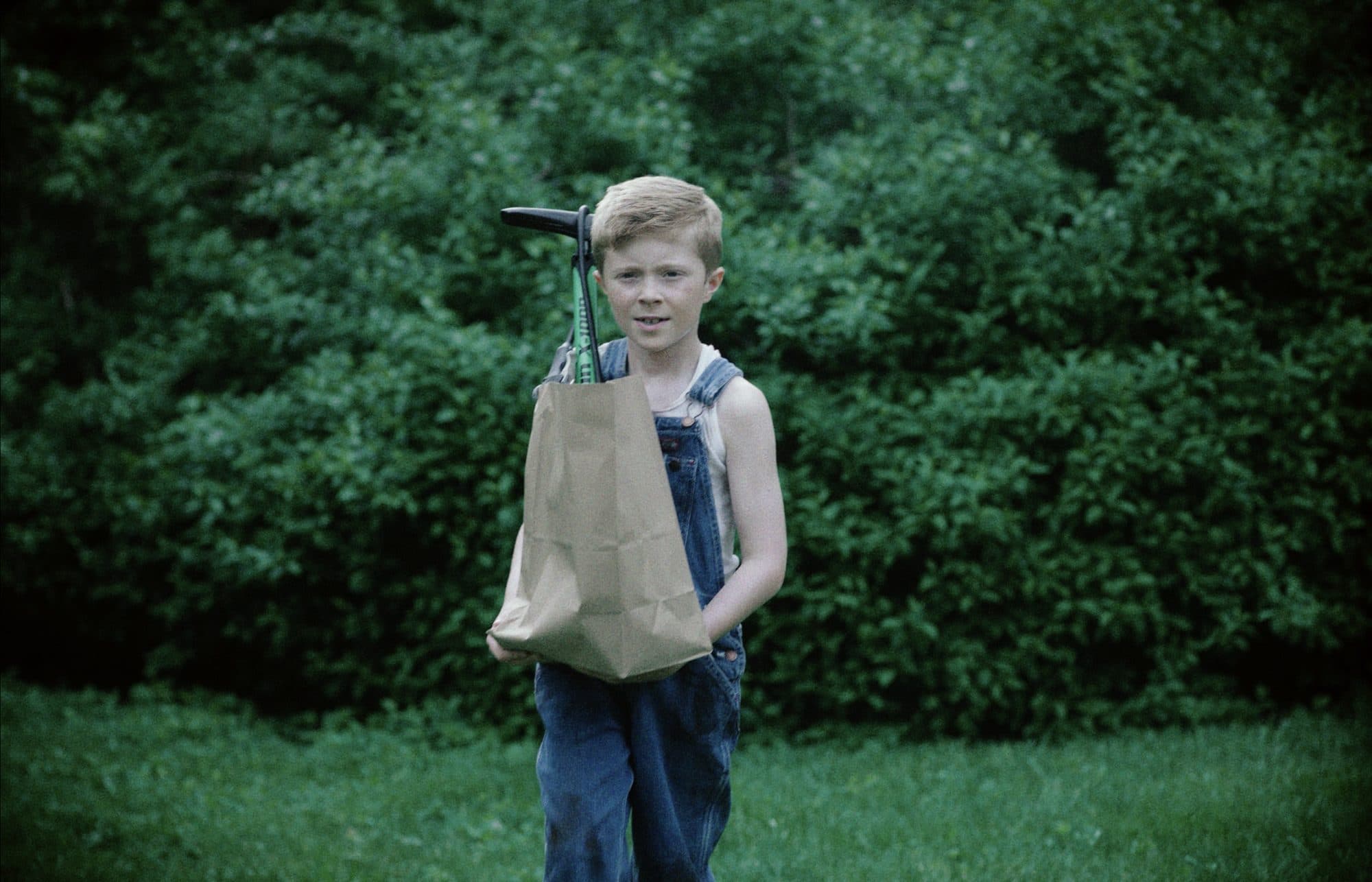 Kaden Stoneking as Willie Valley in overalls holding a paper bag in Elbow Grease